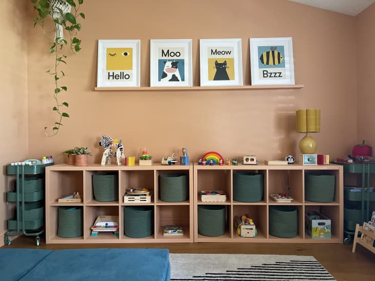 peach cubby storage, teal cubby boxes, teal 3 shelf wheeling storage, hello graphic art, peach walls, floating shelf for pictures, toys, yellow rounded lamp shade, hanging plant, striped black and white rug