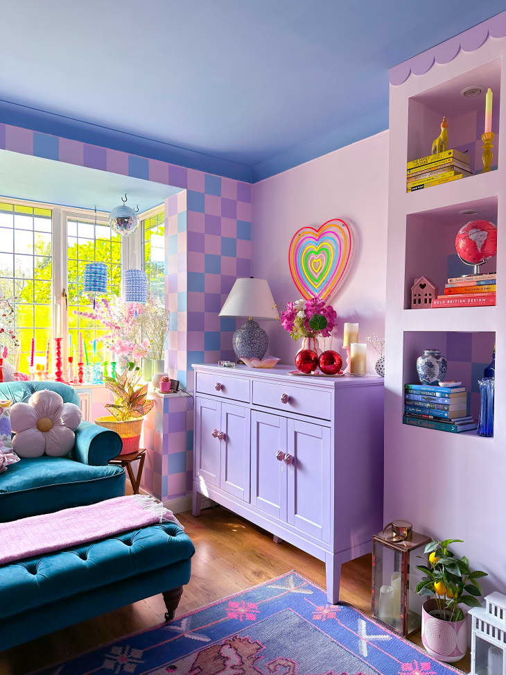 purple blue and pink checkered wall, purple cabinet, heart art, teal velvet loveseat, blue and pink patterned rug, hard wood floors, built in shelving, window, plants