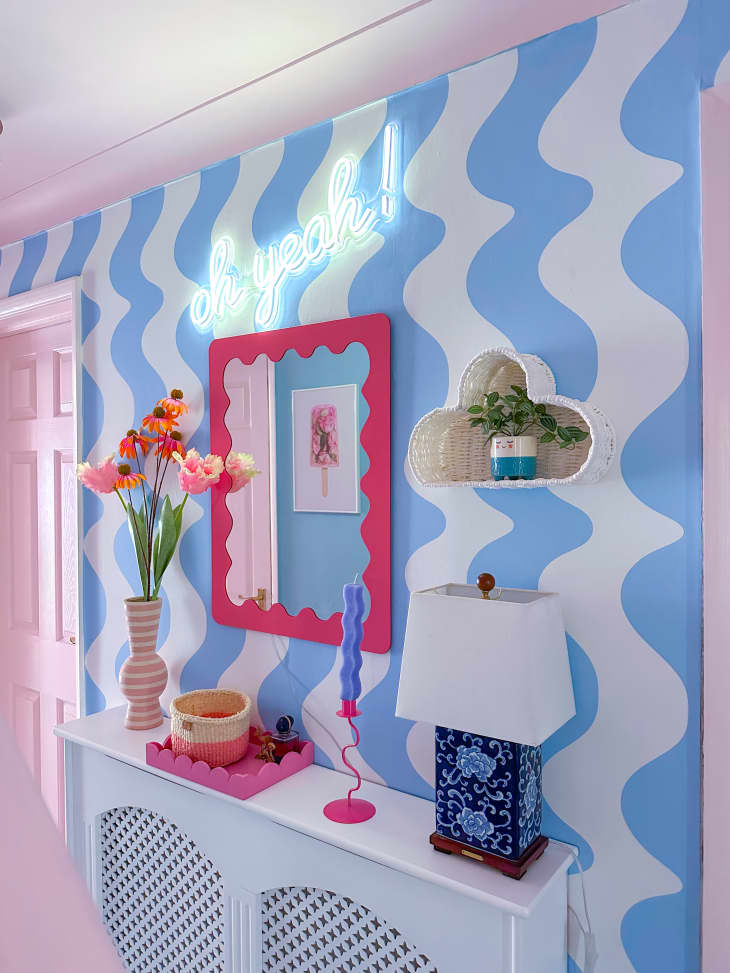 blue wavey striped wall, flowers, pink door, scalloped pink mirror, knickknacks, blue floral pattern lamp
