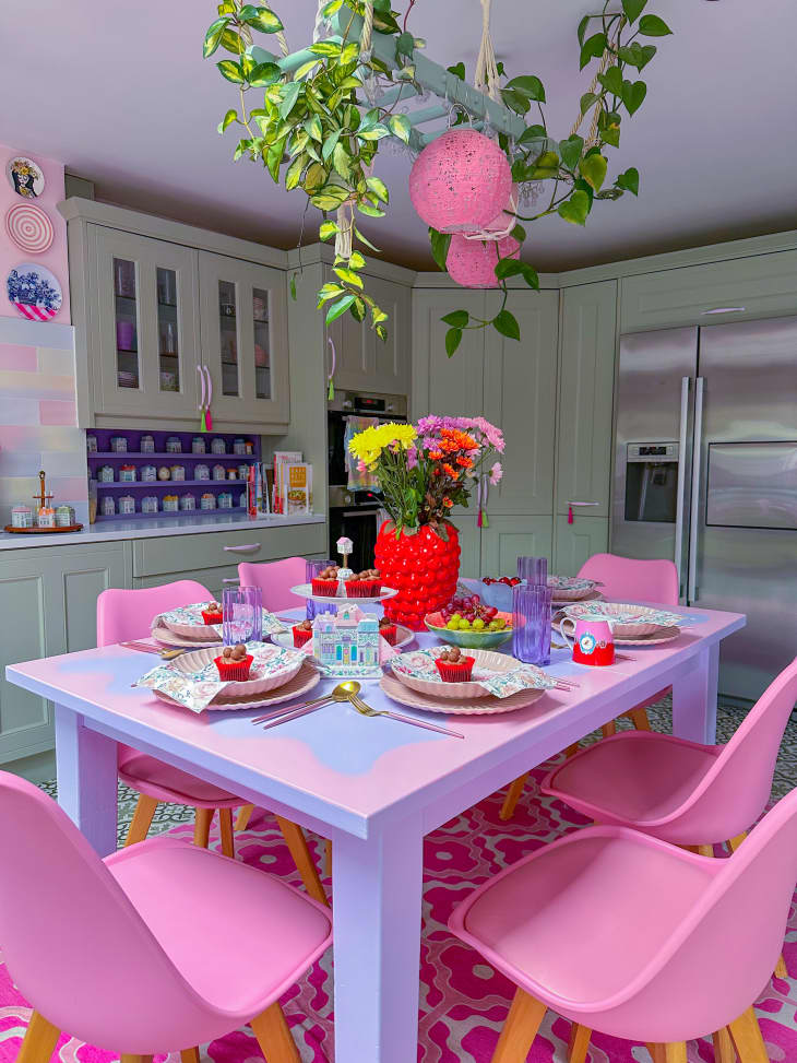 kitchen, sage cabinets, plants, pink and purple flower table, pink chair, pink patterned rug, plants, red vase, cupcakes, table setting