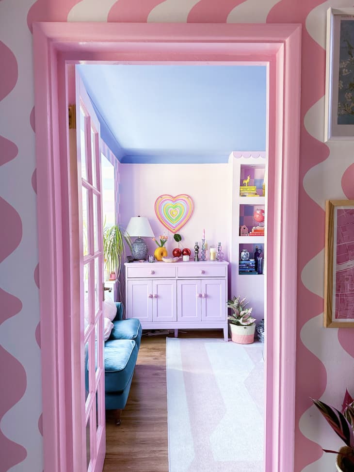 pink door frame, wavy pink stripe walls, purple cabinet, heart art, sunlight, teal velvet loveseat, pink and white rug, hard wood floor, knickknacks, blue ceiling