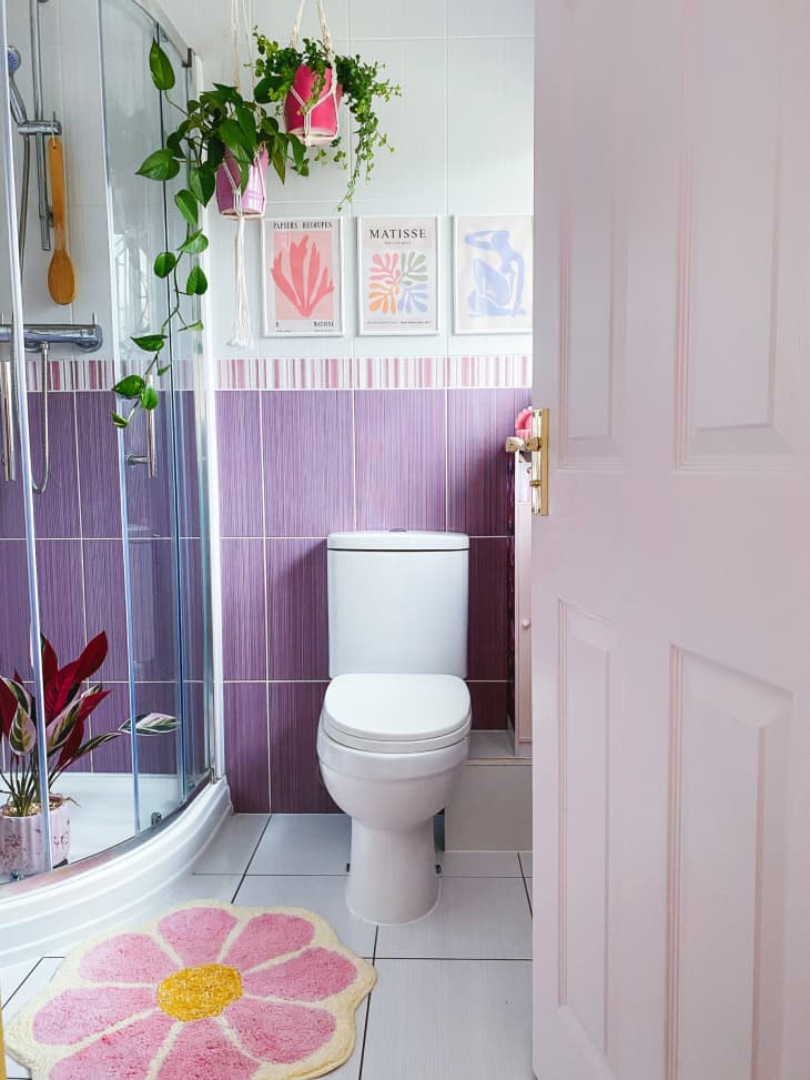 purple tile, half wall tile, standing shower, flower shower rug, white toilet, plants, curved shower door, glass shower door