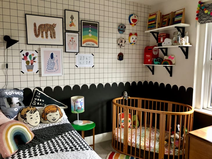 graphic grid on upper half of wall, scallop wall divide, black bottom half of wall, oval baby crib with wooden slates, kids bed, avocado throw pillow, face throw pillows, gallery wall, floating shelves, small green side table, illustrated lamp shade, black and white comforter
