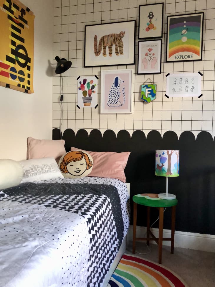 rainbow rug, grid on upper wall, scallop trim half way down wall, black bottom half of wall, black and grey comforter, face throw pillow, pink throw pillow, graphic art, gallery wall, kid's art, illustrated lamp shade, small green side table