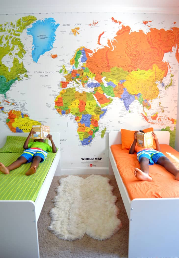 two white wood twin beds, big colorful map, map mural, beige carpet, white faux fur rug, orange and green sheets