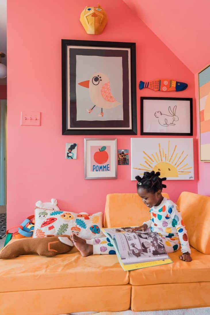 pink wall, yellow orange couch, bold art, gallery wall, angled ceiling, kids pillow