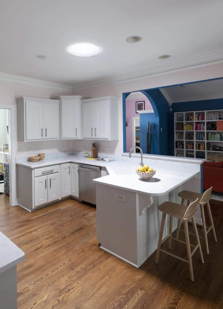 kitchen, white cabinet, white counters, open floor plan, bar stools, wood floors, wall of book shelves, blue arch