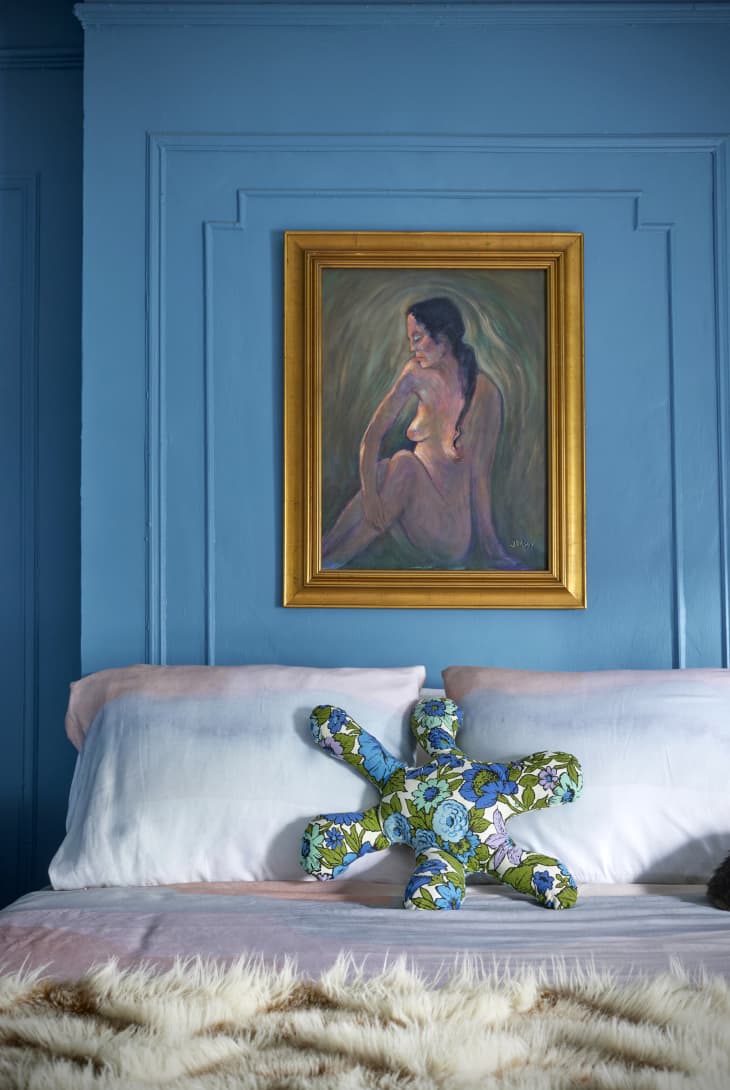 detail of top of bed with blue wainscoting wall behind with nude painting in gold frame
