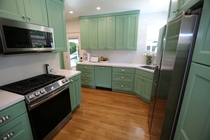 Green cabinets in newly renovated kitchen with white stone countertops and stainless steel appliances.