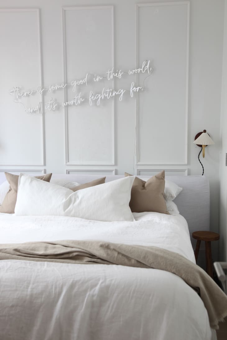 Plug in wall mounted sconce beside neutral colored bed. Neon sign above bed reads " There is some good in this world, and it's worth fighting for".