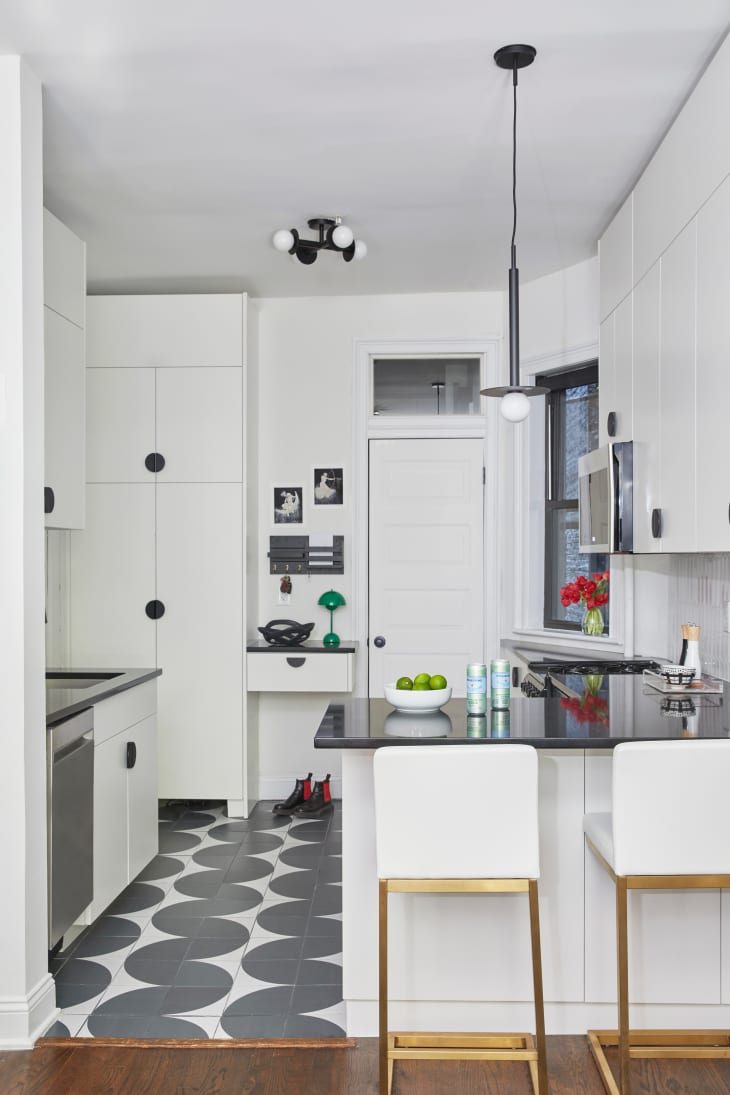 Black and white floor tiles in newly renovated kitchen with black pendant hanging over black bar surface. White countertops with black hardware throughout.