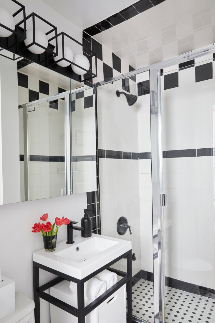 Newly renovated black and white tiled bathroom with glass shower door and small black and white vanity.