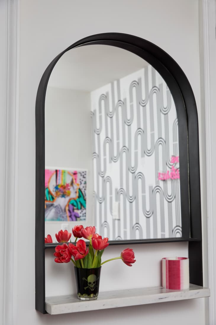 Rounded mirror with small floral arrangement on shelf below in living room.