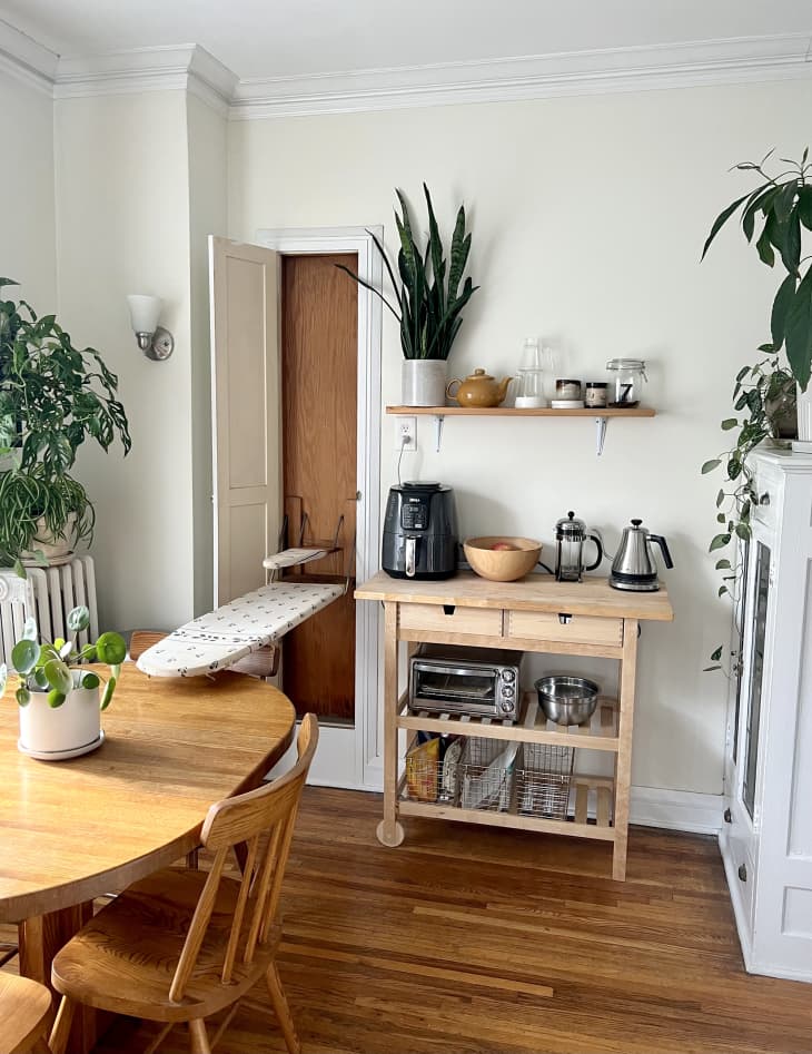 detail of small wood portable kitchen island in dining area with coffee making appliances, toaster oven, steel baskets for storage. part of wood dining table and chairs in view