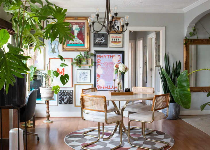 dining room with gray walls, dark bronze chandelier, marble round table with metal legs, rattan backed dining chairs with pale neutral cushions and metal legs, wood floor, round patterned area rug, gallery wall