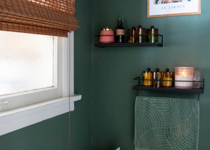 detail of floating shelves in bathroom with lotion, shampoo, etc bottles, candle. Walls are green