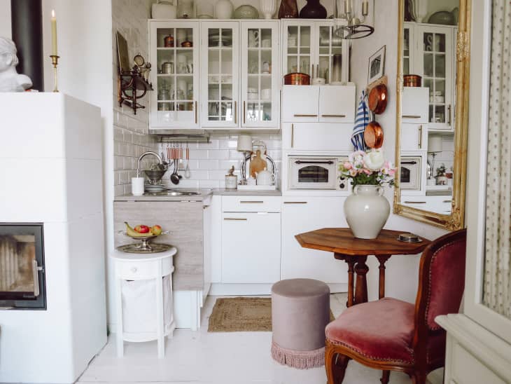 White kitchen with white cabinets, backsplash, small wood dining table with one vintage wood and velvet chair, large gold frame mirror