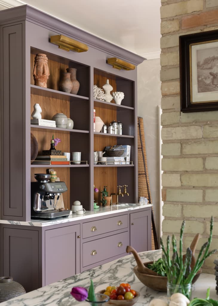 Built in shelving with espresso maker and brass faucet on lower shelf and ceramics and other decorative objects stored above.