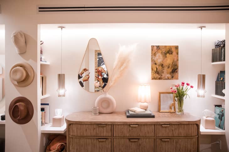 Large dresser in recessed area in bedroom with shelves, art, teardrop mirror, flowers, hats hanging on wall