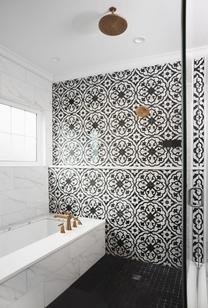 bathtub and wet room style shower behind glass door. Shower tile wall is black and white patterned, gold/brass hardware