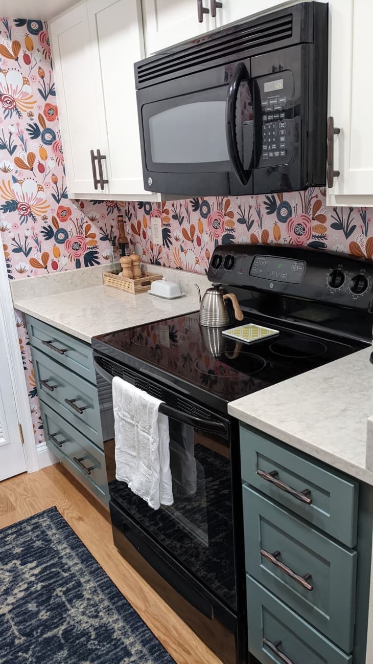 Kitchen with pink floral wall paper, green cabinets and white countertops.