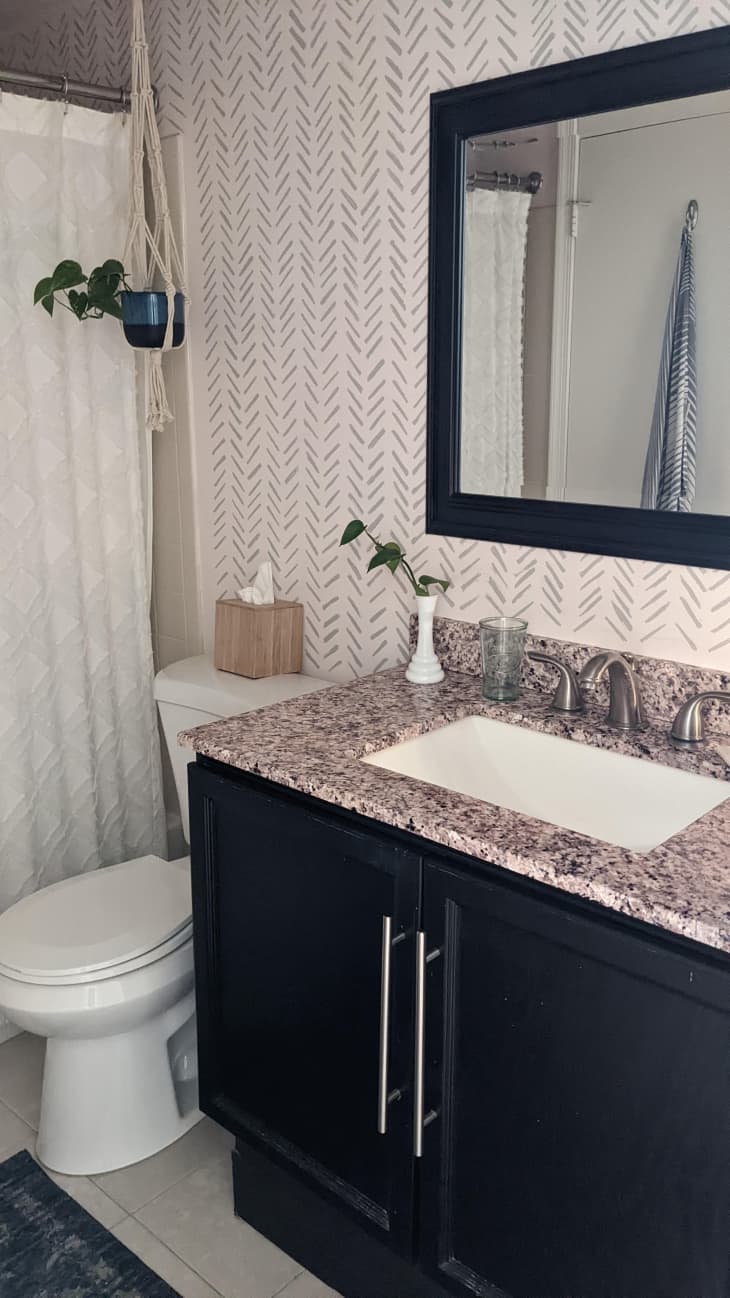 Bathroom with dark cabinets and light colored graphic wallpaper.