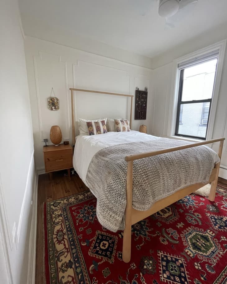 Bedroom with wood frame bed, red patterned rug, white walls, white ceiling fan