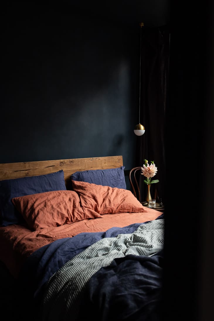 Bedroom with matte black walls, wooden bed board and terra cotta and blue bedding.