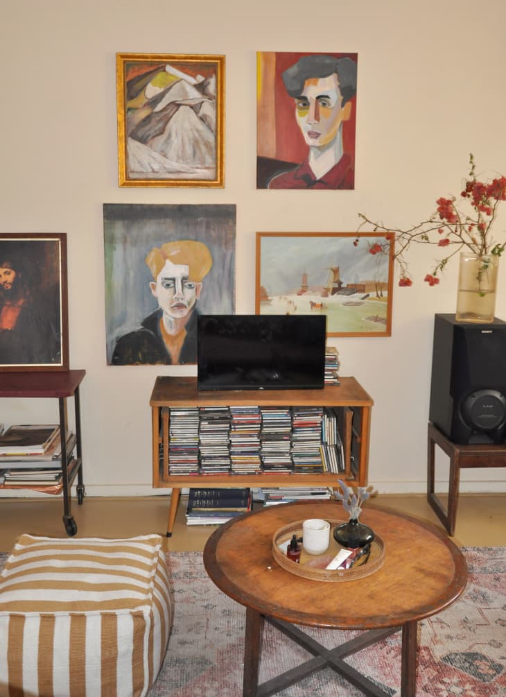 living room with mix of thrifted and hand-painted artwork, round coffee table, small media console with tv