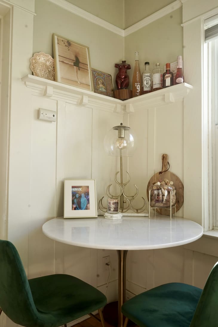 Corner with small white round table, green chairs, shelf overhead