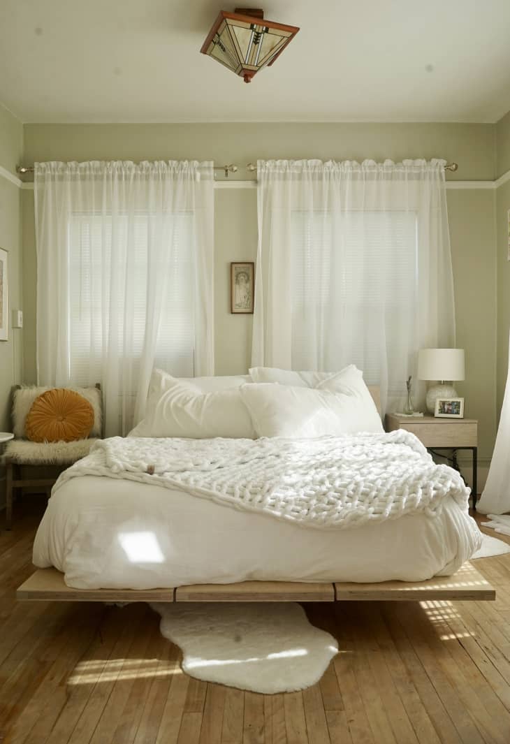 bedroom with pale green walls, white tall curtains, white bed/bedding, wood floor
