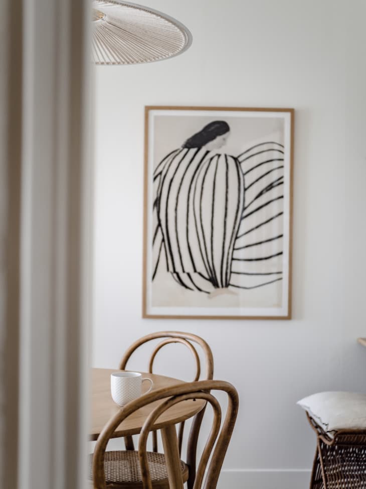 Apartment dining room with lots of white, natural wood, natural colors, natural fiber textiles. Detail of black and white art on wall
