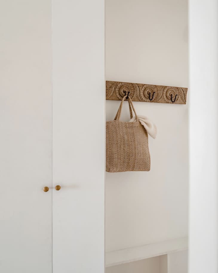 Apartment entryway with lots of white, natural wood, natural colors, natural fiber textiles. Detail of purse hooks