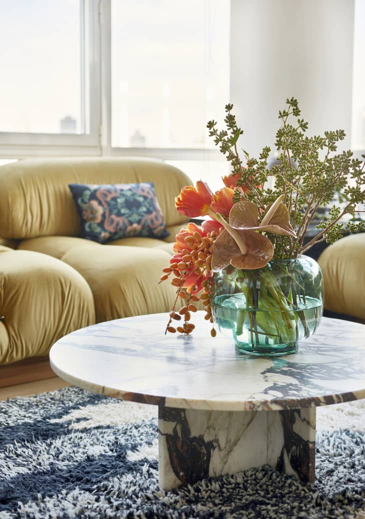 Living room with gold cozy sofa, round marble coffee table, aqua vase with large bouquet of flowers, shag rug