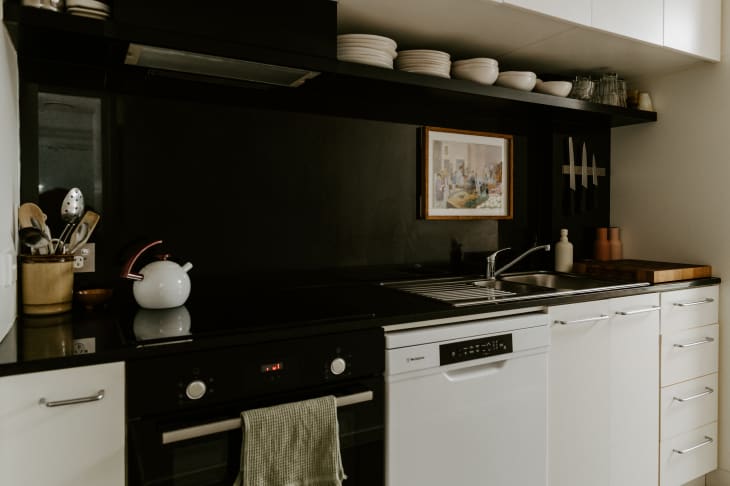 Kitchen with white cabinets and black painted walls. White accents litter the room.
