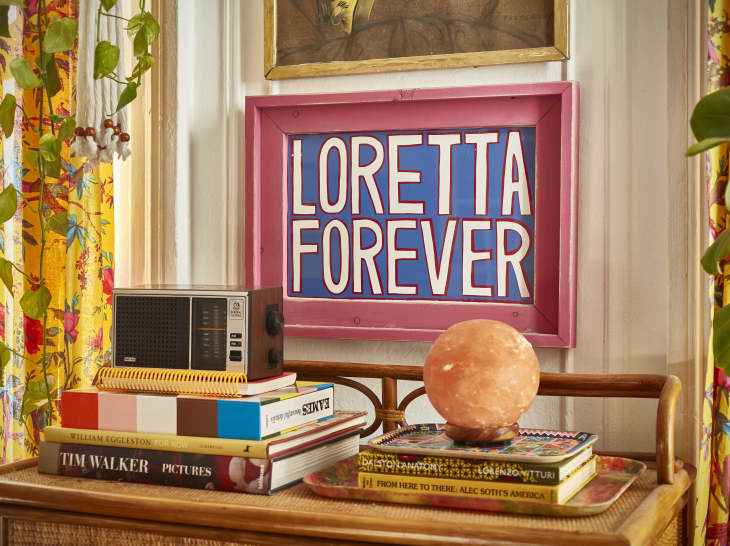 room in colorful Brooklyn apartment--detail of small rattan buffet, art that says "LORETTA FOREVER"