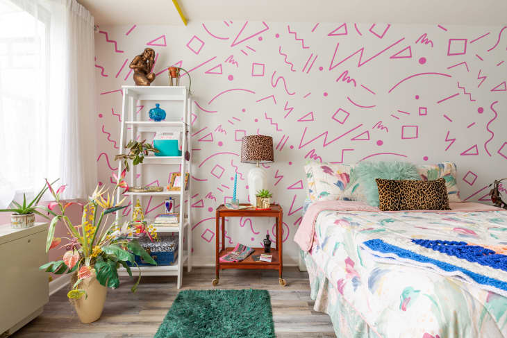 Bedroom with wall with painted pink geometric shapes, bed with pink and mint green pattern bedding