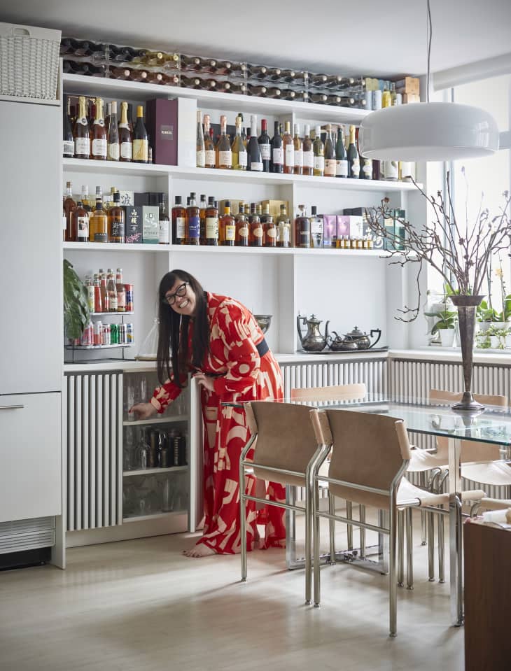 woman in red patterned dress in dining room reaching into a cabinet
