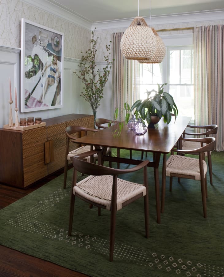 Dining room after makeover. Green rug, mid century wood table and chairs, leaf wallpaper, poster of sunbathing woman and chimp