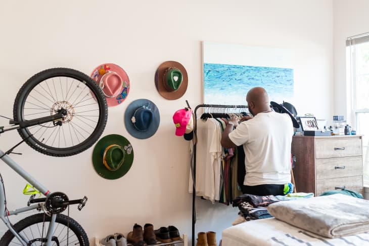 man looking through clothes on a rack in a room with a bicycle, hats on the wall, a dresser, shoe rack