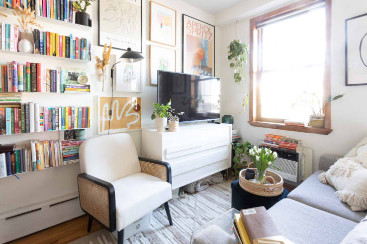 White chair next to media console in living room area of art and book filled studio apartment.