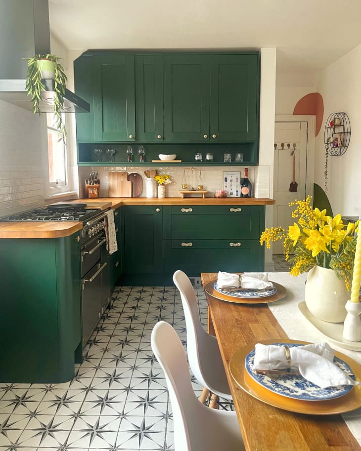 Kitchen with dark green cabinets, white walls, star tile (or linoleum) floor, wood dining table in foreground