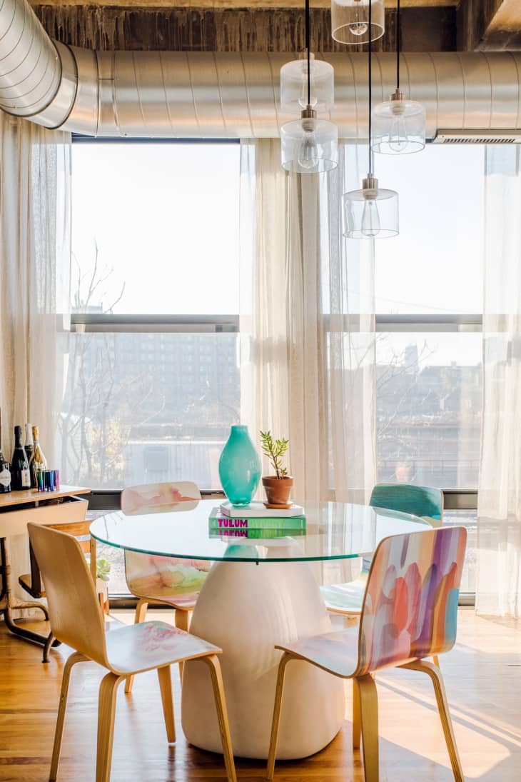 dining room with custom-painted chairs, glass round table, large windows, glass pendant lights