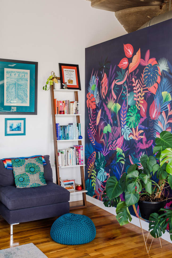 Corner of living space with cozy accent chair, colorful plant mural, art, books, fireplace