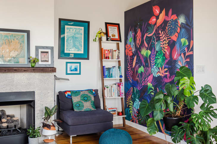 Corner of living space with cozy accent chair, colorful plant mural, art, books, fireplace