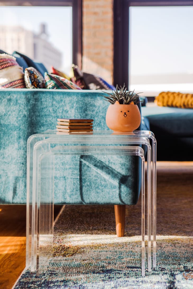 detail of lucite stacking tables next to a blue sofa. terracotta cat planter with cactus