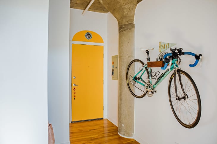 Bicycle hanging on rack on wall. View of front door, painted bright yellow