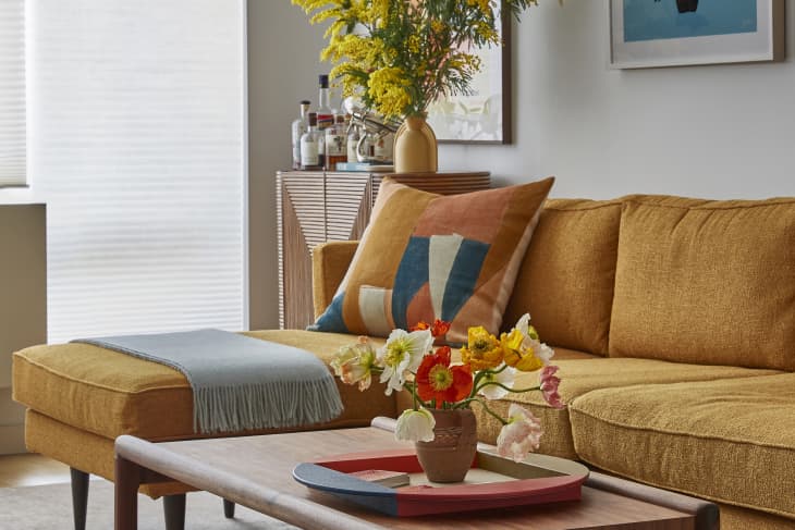 living room with gold/orange sofa, fresh colorful flowers, pops of color via art. textiles