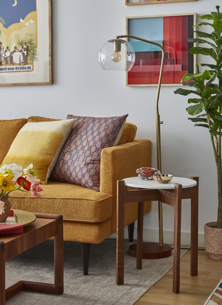 living room with gold/orange sofa, fresh colorful flowers, pops of color via art. textiles
