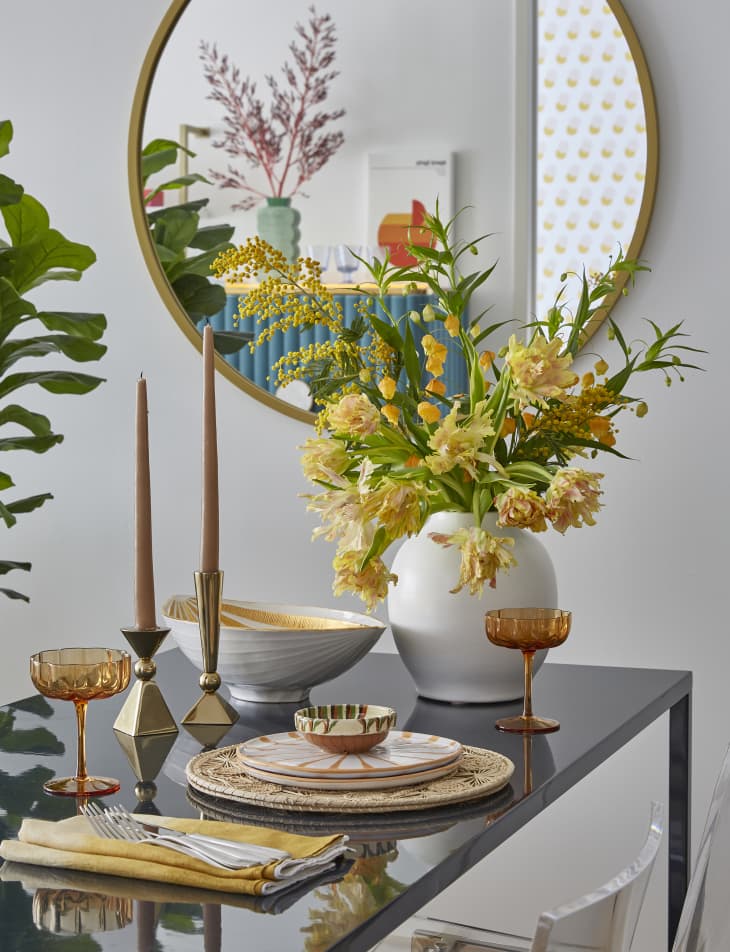 table with orange and white place setting, white vase with yellow and orange flowers, round mirror